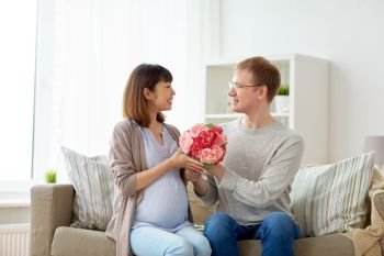 pregnancy, holidays and people concept - happy husband giving flowers to his pregnant wife for birthday at home. happy husband giving flowers to his pregnant wife