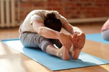 fitness, sport and healthy lifestyle concept - man doing yoga seated forward bend pose on mats at studio or gym. man doing yoga forward bend at studio or gym