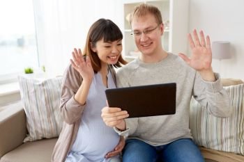 pregnancy, technology and people concept - happy husband and his pregnant wife with tablet pc computer having video chat at home. husband and pregnant wife with tablet pc at home