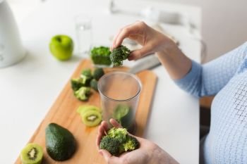 healthy eating, baby food, diet and cooking concept - close up of woman hand adding broccoli to measuring cup with spinach. woman hand adding broccoli to measuring cup