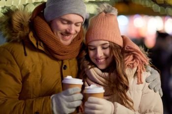 winter holidays, hot drinks and people concept - happy young couple with coffee over christmas lights in evening. happy couple with coffee over christmas lights