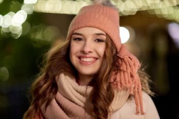 holidays and people concept - portrait of beautiful happy young woman over christmas lights in winter evening. happy young woman over christmas lights in winter