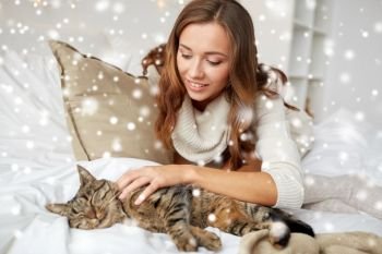 pets, comfort, winter and people concept - happy young woman with cat lying in bed at home over snow. happy young woman with cat lying in bed at home