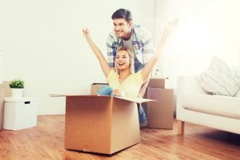 home, people, moving and real estate concept - happy couple having fun and riding in cardboard boxes at new home. happy couple having fun with boxes at new home