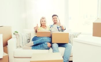 moving, people, repair and real estate concept - happy couple with big cardboard boxes showing thumbs up on sofa at new home. happy couple with boxes showing thumbs up at home