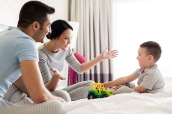 people and family concept - happy child with toy tractor and parents playing in bed at home or hotel room. happy family in bed at home or hotel room