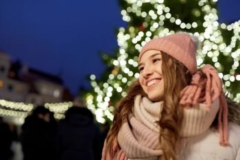 holidays and people concept - portrait of beautiful happy young woman at christmas tree in winter evening. happy young woman at christmas market in winter