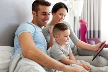 people, family and technology concept - happy mother, father and little boy with tablet pc computer in bed at home or hotel room. happy family with tablet pc in bed at home