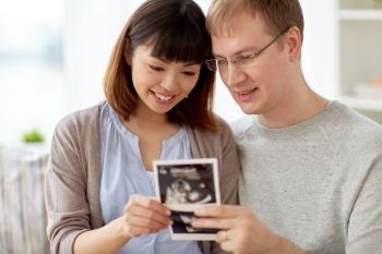 pregnancy, family and people concept - close up of happy couple looking at baby ultrasound images at home. close up of happy couple with baby ultrasound