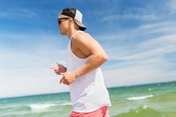 fitness, sport, people and healthy lifestyle concept - happy young man running along summer beach. happy man running along summer beach