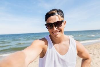summer holidays and people concept - happy smiling young man in sunglasses and hat taking selfie on beach. man in sunglasses taking selfie on summer beach