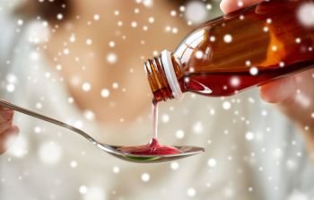 healthcare, people and medicine concept - woman pouring medication or antipyretic syrup from bottle to spoon over snow. woman pouring medication from bottle to spoon