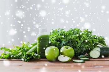 healthy eating, food, diet and vegetarian concept - bottle with green juice, fruits and vegetables on wooden table over snow. close up of bottle with green juice and vegetables