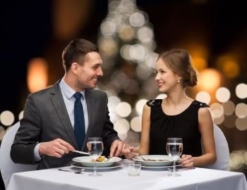 people and holidays concept - smiling couple eating main course at restaurant over christmas tree background. smiling couple eating at christmas restaurant