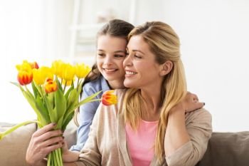 people, family and holidays concept - happy girl giving tulip flowers to her mother at home. happy girl giving flowers to mother at home