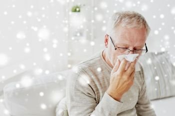 healthcare, flu, hygiene and people concept - sick senior man with paper wipe blowing his nose at home over snow. sick senior man with paper wipe blowing his nose