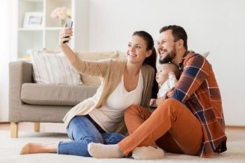 family, parenthood and people concept - happy mother and father with baby taking selfie by smartphone at home. mother and father with baby taking selfie at home