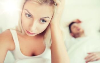 people, health, sleep disorder concept - couple in bed at home, man snoring and young woman suffering from insomnia. awake woman having insomnia in bed