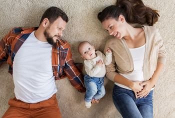 family, parenthood and people concept - happy mother and father with baby lying on floor at home. happy family with baby lying on floor at home