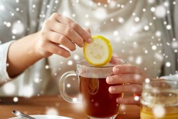 health, traditional medicine and ethnoscience concept - close up of woman adding lemon to tea cup with honey over snow. close up of woman adding lemon to tea with honey