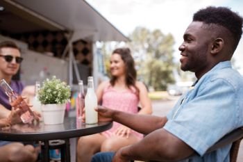 leisure and people concept - happy friends with drinks sitting at table at food truck. friends with drinks sitting at table at food truck