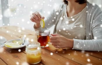 healthy food, eating and ethnoscience concept - close up of ill woman adding honey to tea cup with lemon and ginger over snow. close up of woman adding honey to tea with lemon