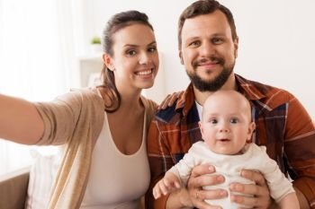 family, parenthood and people concept - happy mother and father with baby taking selfie at home. mother and father with baby taking selfie at home
