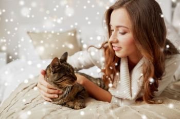 pets, comfort, christmas, winter and people concept - happy young woman with cat lying in bed at home over snow. happy young woman with cat lying in bed at home