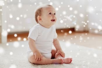 childhood, babyhood and people concept - happy little baby boy or girl sitting on floor with soap bubbles around at home over snow. happy baby with soap bubbles at home
