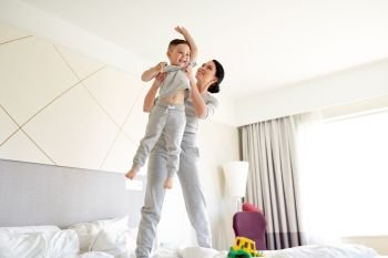 people, family and morning concept - happy mother with little son playing in bed at home or hotel room. happy mother with son in bed at home or hotel room