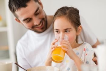 family, eating and people concept - happy father and daughter having breakfast at home. happy girl with father drinking juice at home