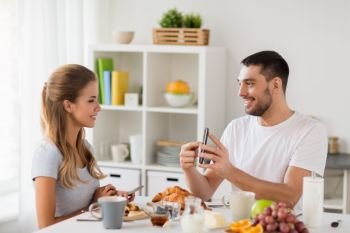 technology, eating and people concept - happy couple with smartphones having breakfast at home. couple with smartphones having breakfast at home