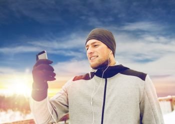 fitness, sport, people, technology and healthy lifestyle concept - happy smiling young man in earphones with smartphone listening to music on winter bridge. happy man with earphones and smartphone in winter