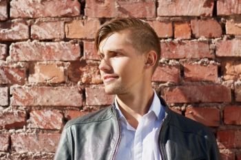 lifestyle and people concept - portrait of young man in leather jacket over brick wall outdoors. portrait of man in leather jacket over brick wall