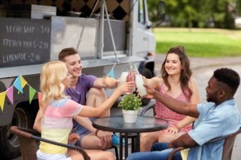 celebration, leisure and people concept - happy friends clinking bottles with drinks at food truck. friends clinking bottles with drinks at food truck