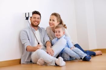 mortgage, technology and real estate concept - happy family with child taking picture by smartphone selfie stick at new home. family taking selfie by smartphone at new home