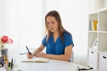 business, people and work concept - middle-aged woman writing to notebook at office or home. woman writing to notebook at office