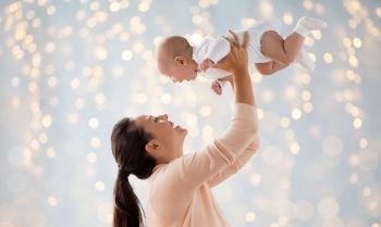 family, motherhood and people concept - happy mother playing with little baby boy over holidays lights background. happy mother playing with little baby over lights
