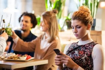 technology, lifestyle and people concept - woman with smartphone and friends at restaurant. woman with smartphone and friends at restaurant