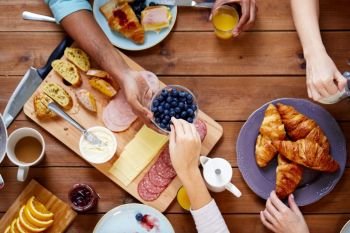 food, eating and family concept - group of people sharing blueberries for breakfast at wooden table. people having breakfast at table with food
