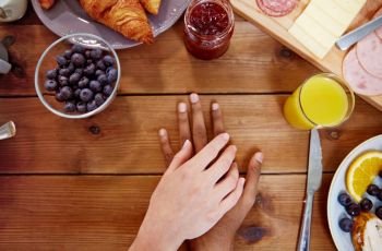 people, relationships and eating concept - multiracial couple holding hands while having breakfast at table full of food. couple hands on table full of food