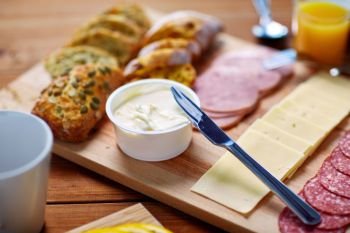 food, catering and eating concept - cream cheese with knife, sliced sausage and bread on wooden table at breakfast. cream cheese and other food on table at breakfast