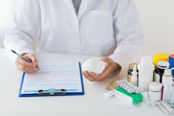 medicine, healthcare and people concept - doctor with drugs and clipboard writing prescription or medical report at hospital. doctor with medicines and clipboard at hospital