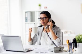 business, technology, communication and people concept - happy smiling businesswoman or secretary calling on phone and drinking coffee at office. businesswoman calling on phone at office