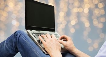 technology and people concept - close up of man typing on laptop keyboard over holidays lights background. close up of man typing on laptop keyboard