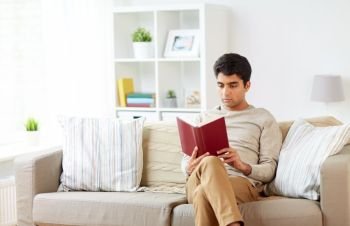 leisure, literature and people concept - man sitting on sofa and reading book at home. man sitting on sofa and reading book at home