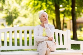 old age, retirement and people concept - sad senior woman sitting on bench at summer park. sad senior woman sitting on bench at summer park