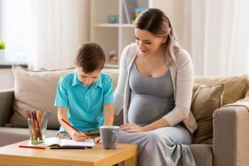 family, education and pregnancy concept - happy pregnant mother and little son with workbook writing or drawing at home. pregnant mother and son with workbook at home