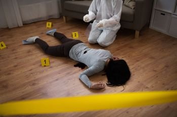 investigation and forensic examination concept - criminalist collecting evidence of murder of woman at crime scene fenced by police tape (staged photo). criminalist collecting evidence at crime scene