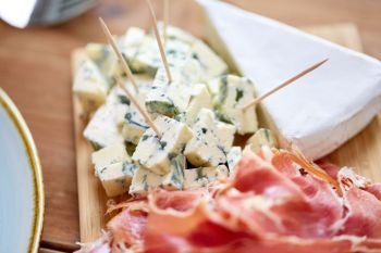 food, catering and eating concept - blue cheese and jamon or parma ham on wooden board. blue cheese and jamon or parma ham on wooden board
